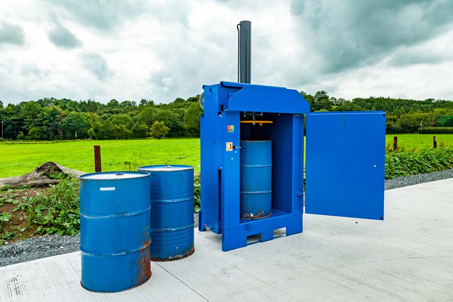 a drum crusher with empty oil barrels ready to be compacted.